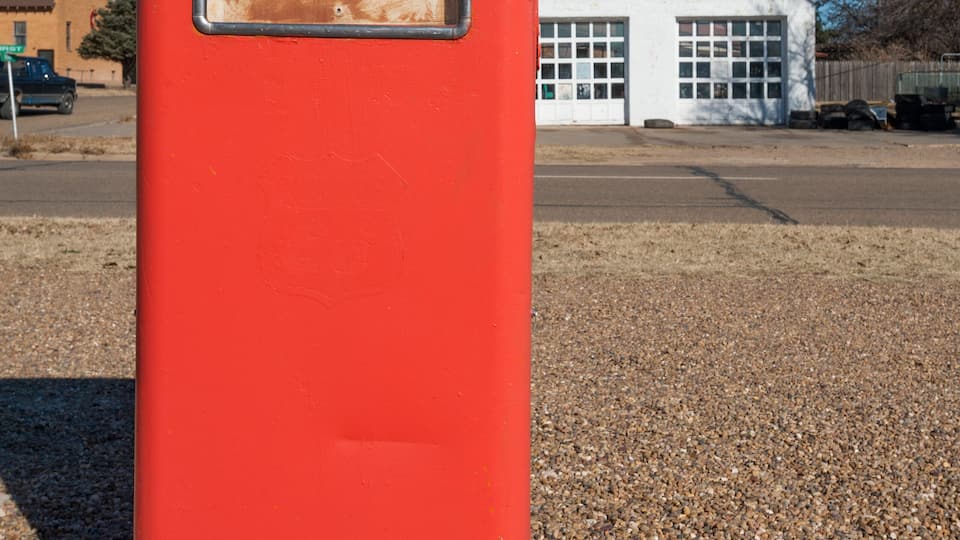 A red gas pump with a price sign in front of a white building.
