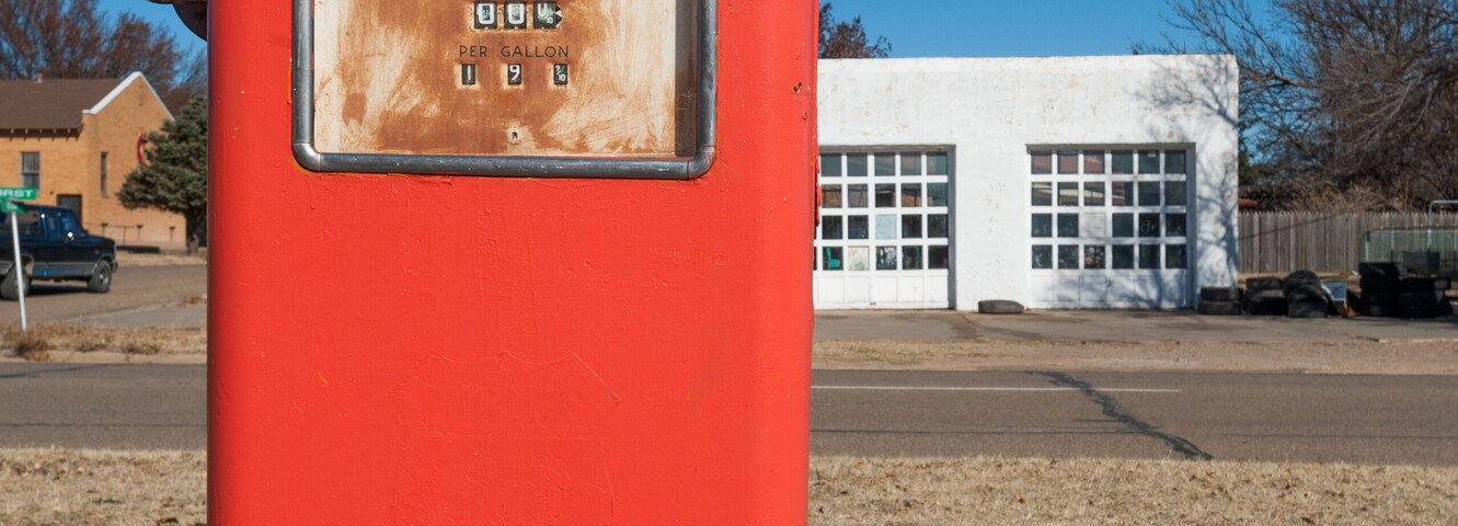 Uma bomba de gasolina vermelha com um letreiro de preços em frente a um edifício branco.