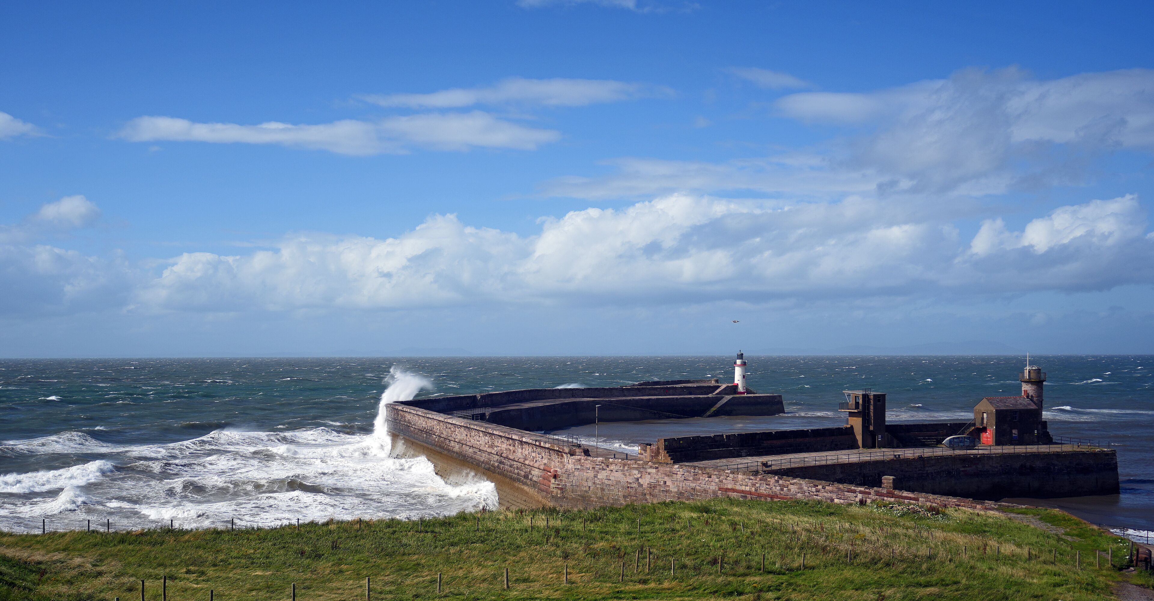 A coastal lighthouse and breakwater with waves crashing against it.