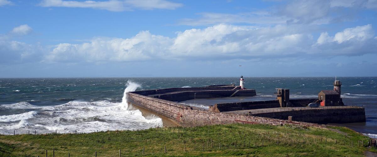 A coastal lighthouse and breakwater with waves crashing against it.