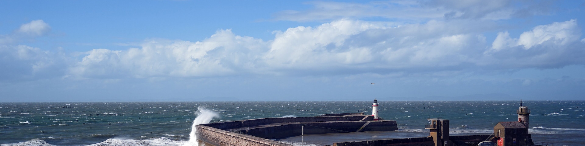 A coastal lighthouse and breakwater with waves crashing against it.