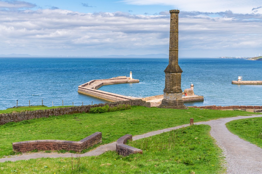 A lighthouse and a tall chimney by the sea.