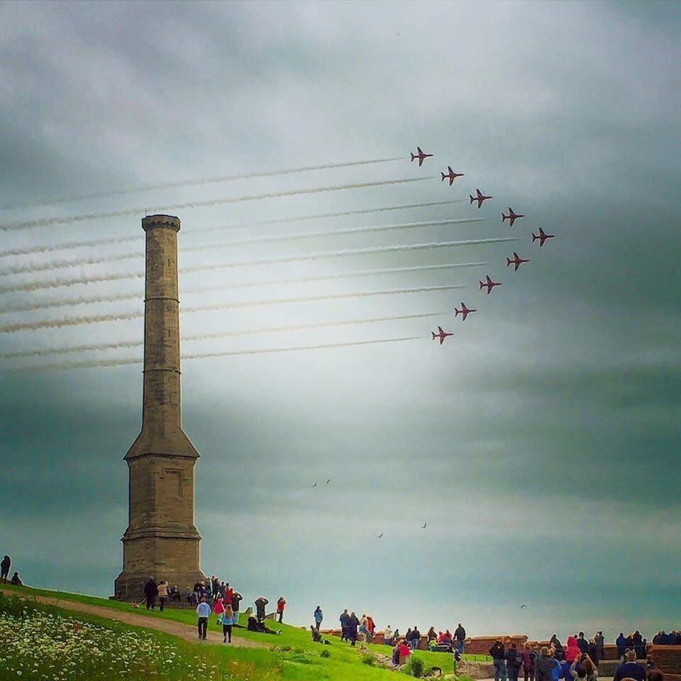 A monument with a crowd of people and a formation of jets flying overhead.