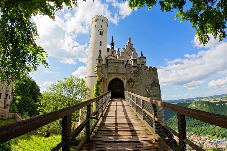 Un castello con una torre, un ponte di legno e un paesaggio montuoso.