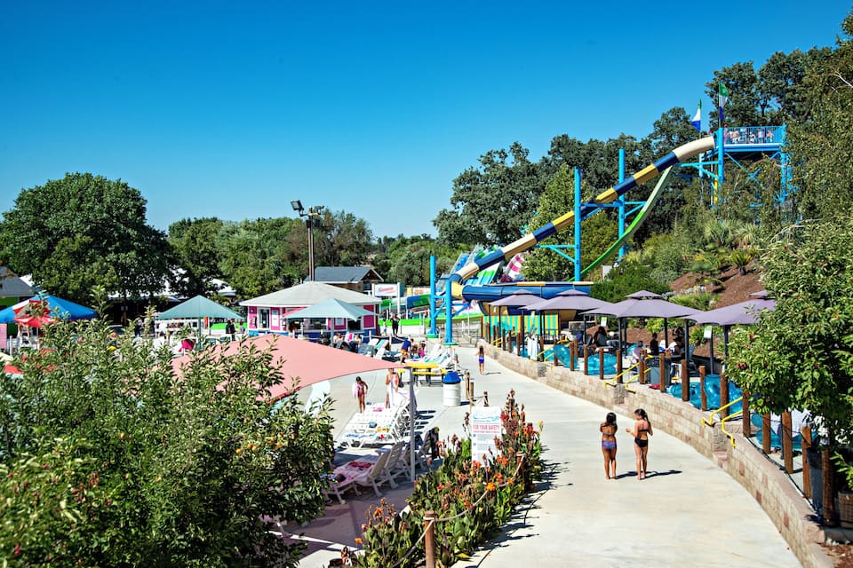 Een waterpark met een glijbaan, zitplaatsen bij het zwembad en parasols.