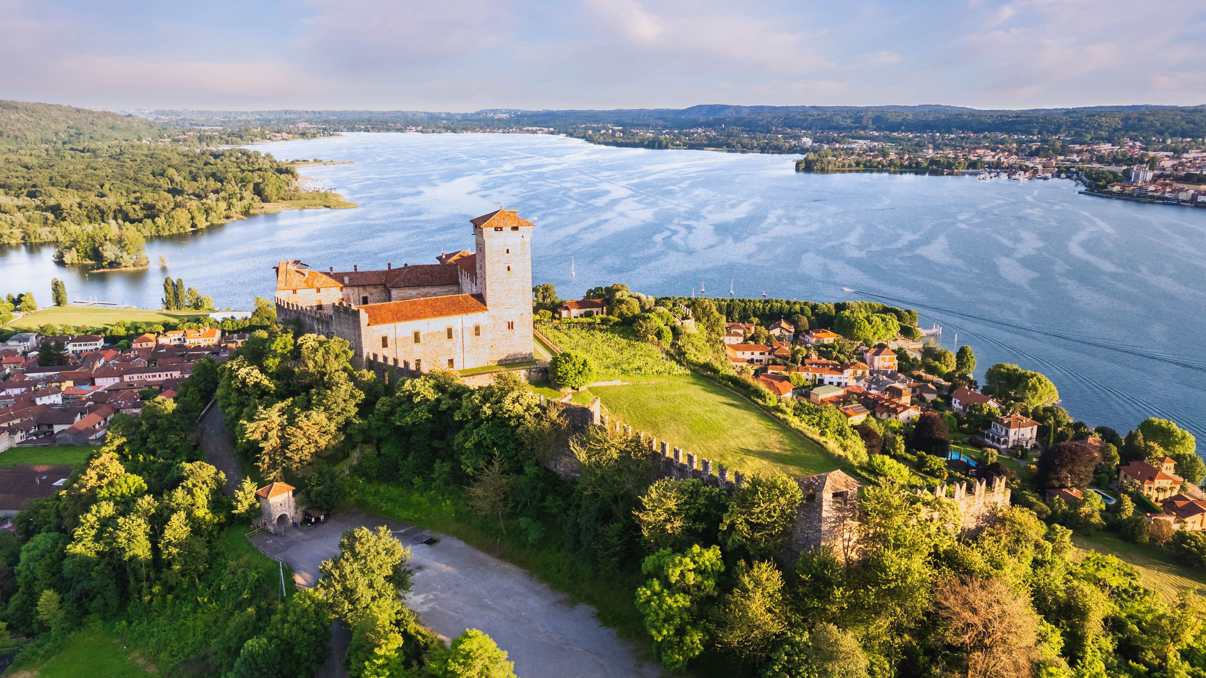 A castle on a hill overlooking a river, surrounded by greenery and a small town.