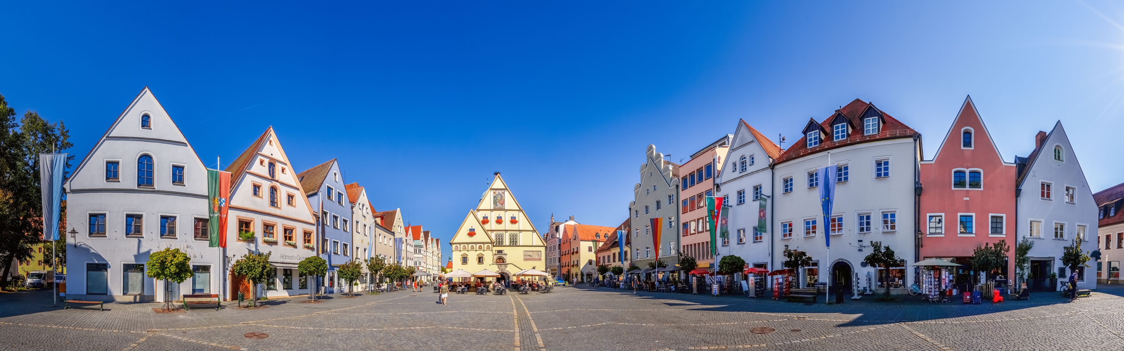 A cobblestone square with historic buildings, a prominent church, and flags.