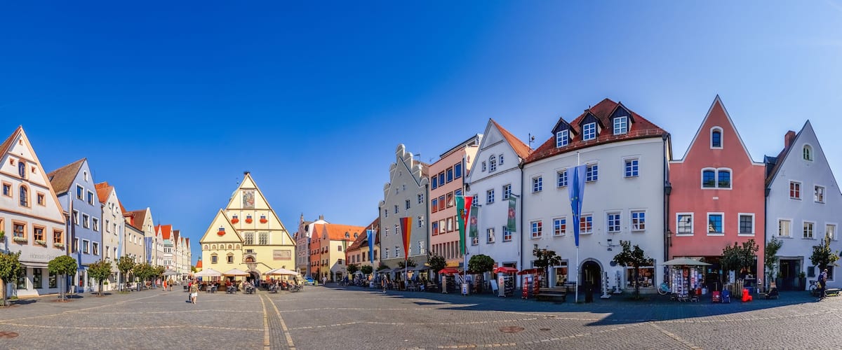 A cobblestone square with historic buildings, a prominent church, and flags.