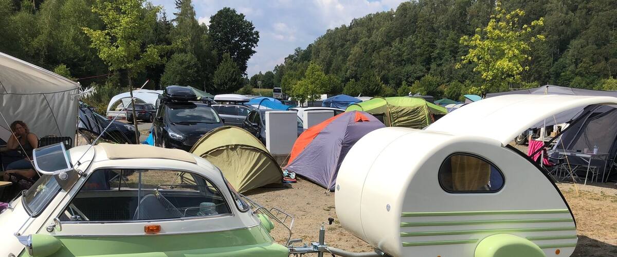 A vintage camper parked next to a green car, surrounded by tents and other vehicles in a camping area.
