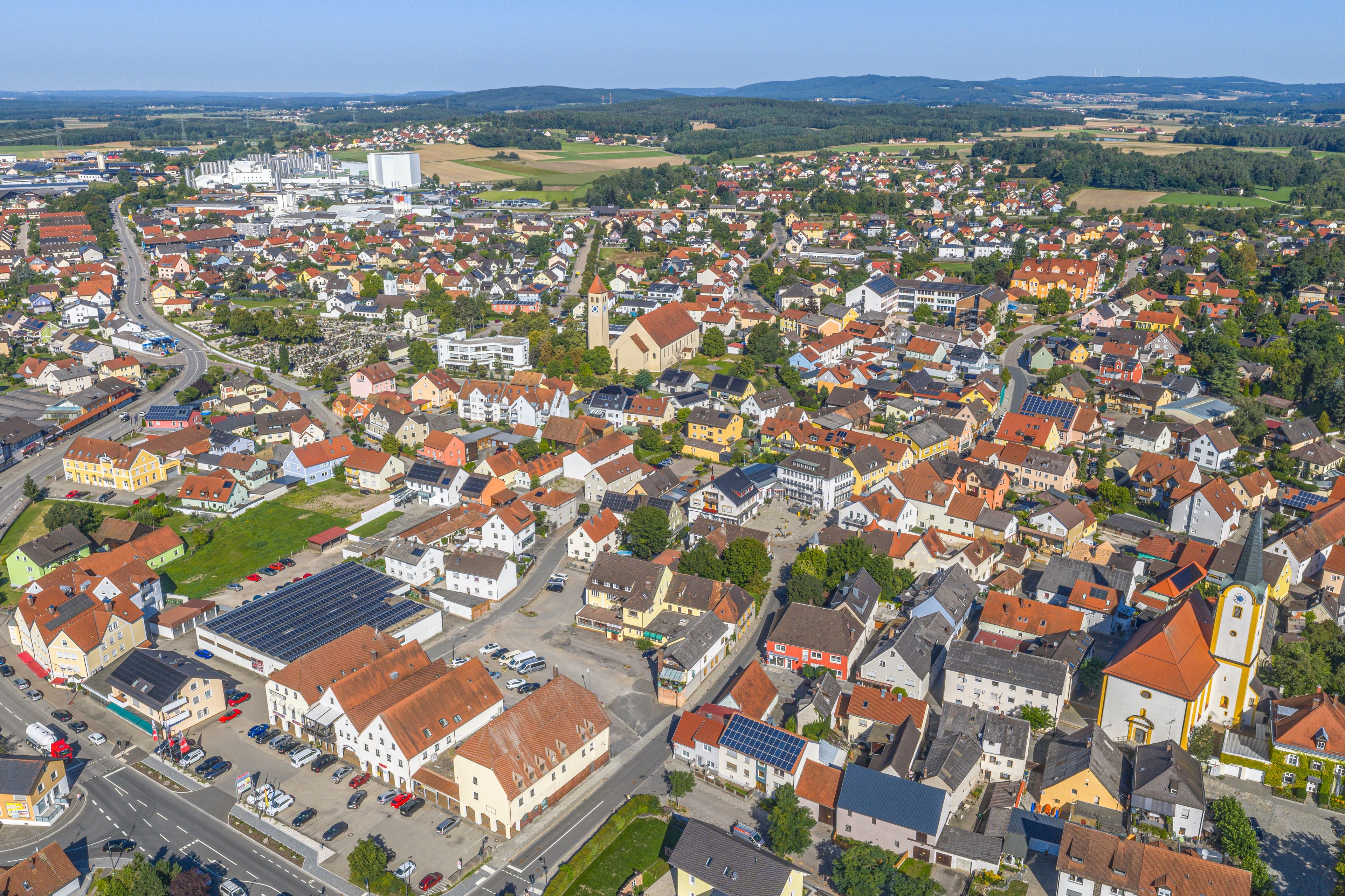 A densely populated town with a mix of residential and commercial buildings, a prominent church tower, and a large industrial facility in the background.