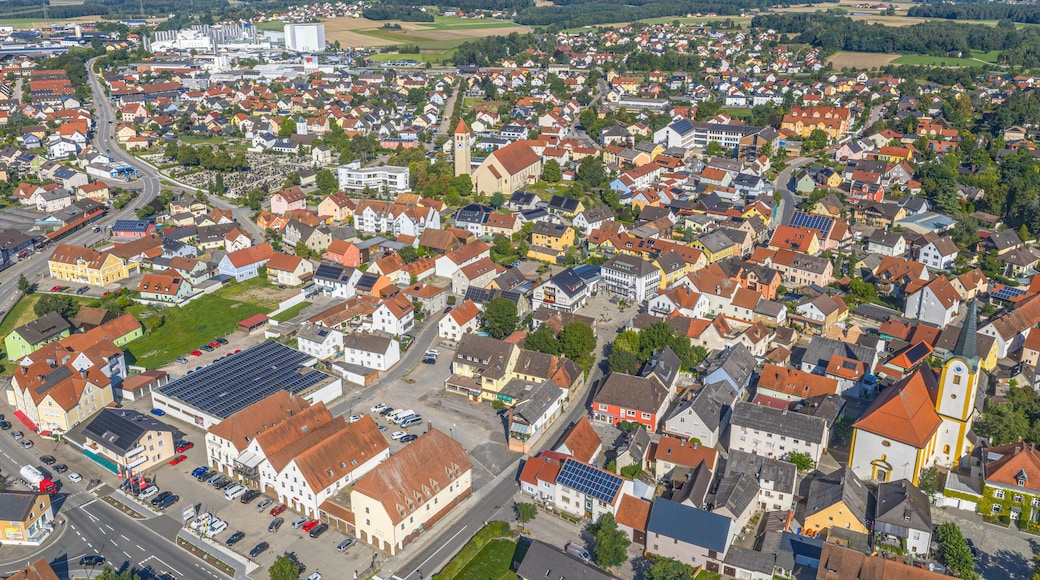 A densely populated town with a mix of residential and commercial buildings, a prominent church tower, and a large industrial facility in the background.