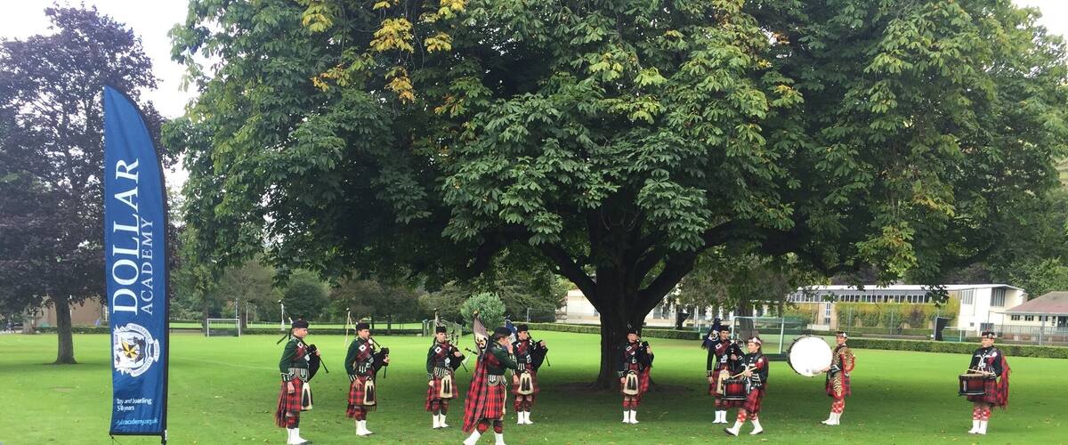 A group of bagpipers performing in a grassy area with a blue flag in the background.