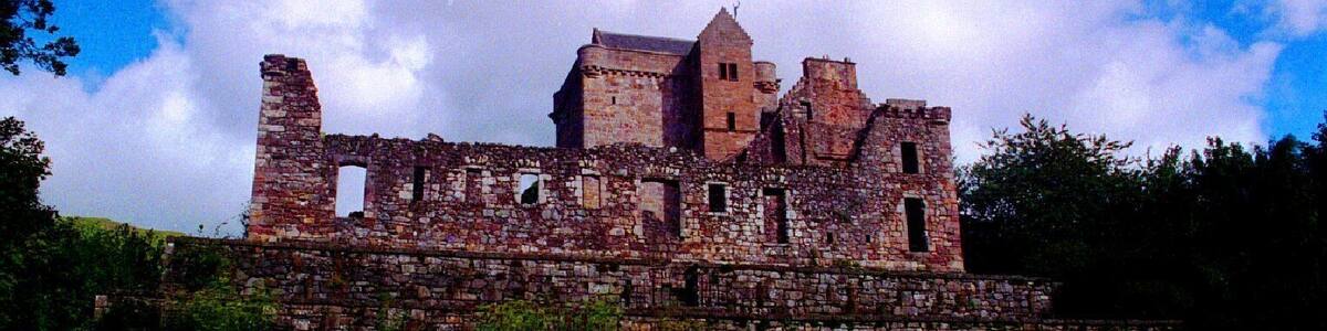 Eine historische Burg aus Stein mit Ruinen, umgeben von üppigem Grün und Bäumen.