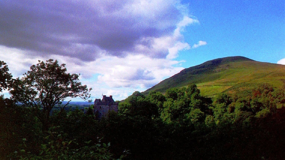 A castle on a hill with lush greenery and a partly cloudy sky.