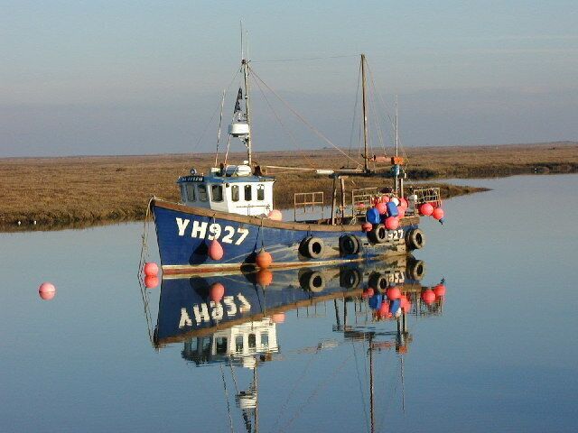A boat with the registration number YH927 anchored in calm waters, surrounded by a flat landscape.