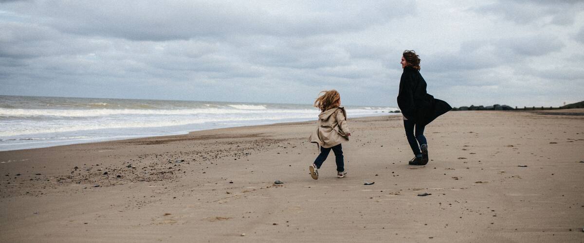 A beach with a child and an adult walking along the shore.