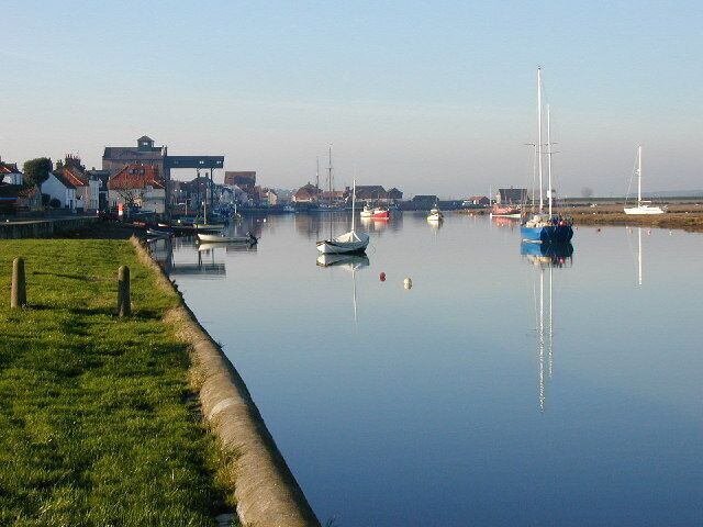 A calm river with boats, a grassy bank, and buildings in the background.