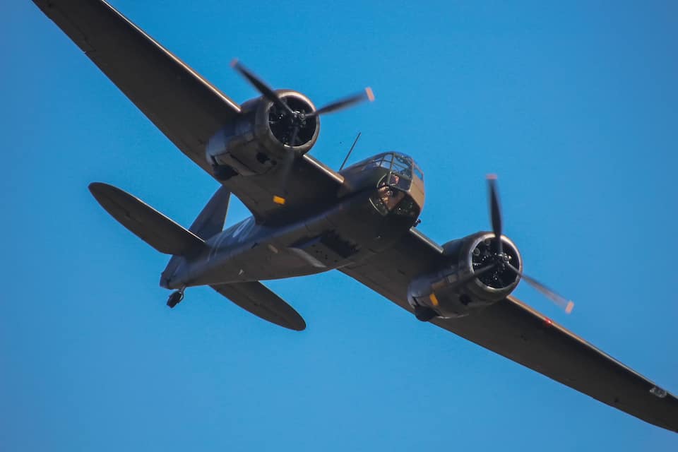 A large military aircraft with four propellers flying against a clear blue sky.