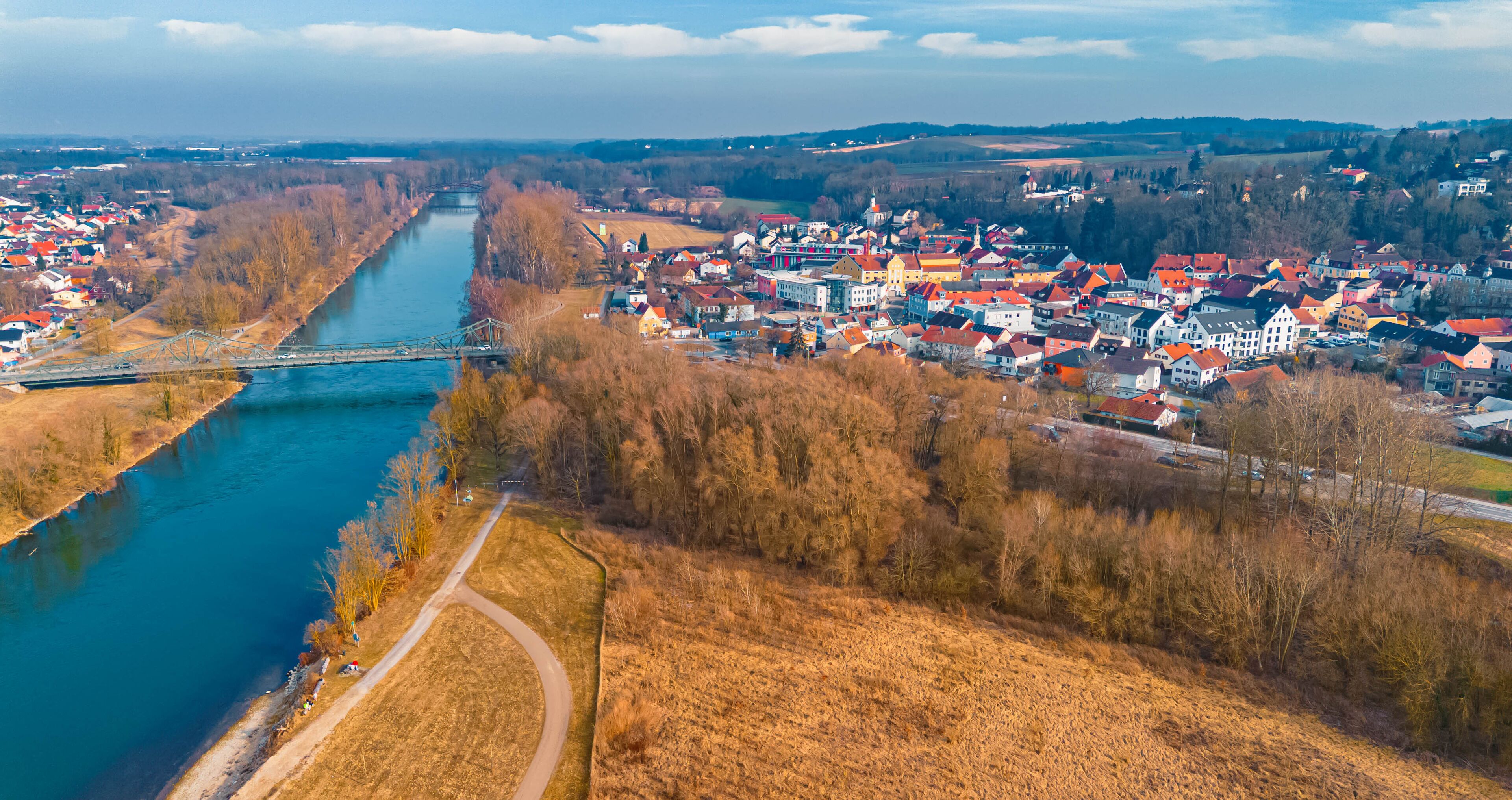 A river flowing through a town with a bridge, surrounded by fields and trees.