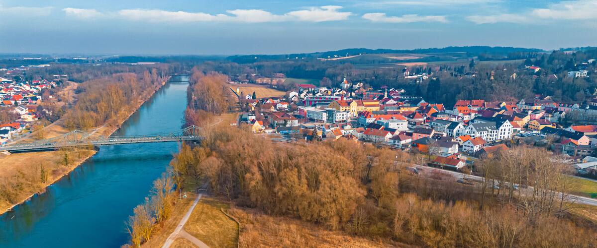 A river flowing through a town with a bridge, surrounded by fields and trees.