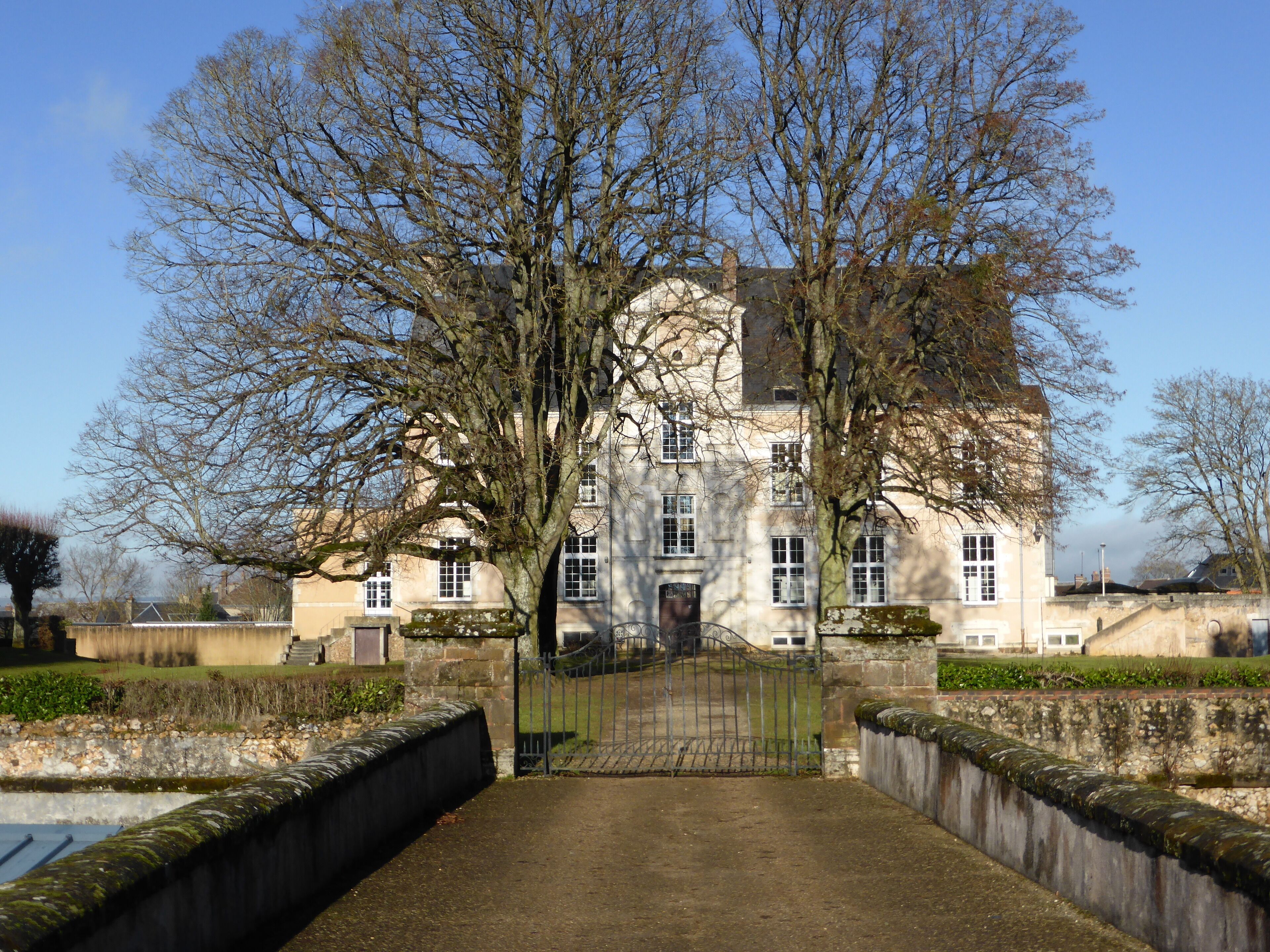 A large, historic building with a symmetrical facade, surrounded by a formal garden and a stone wall.