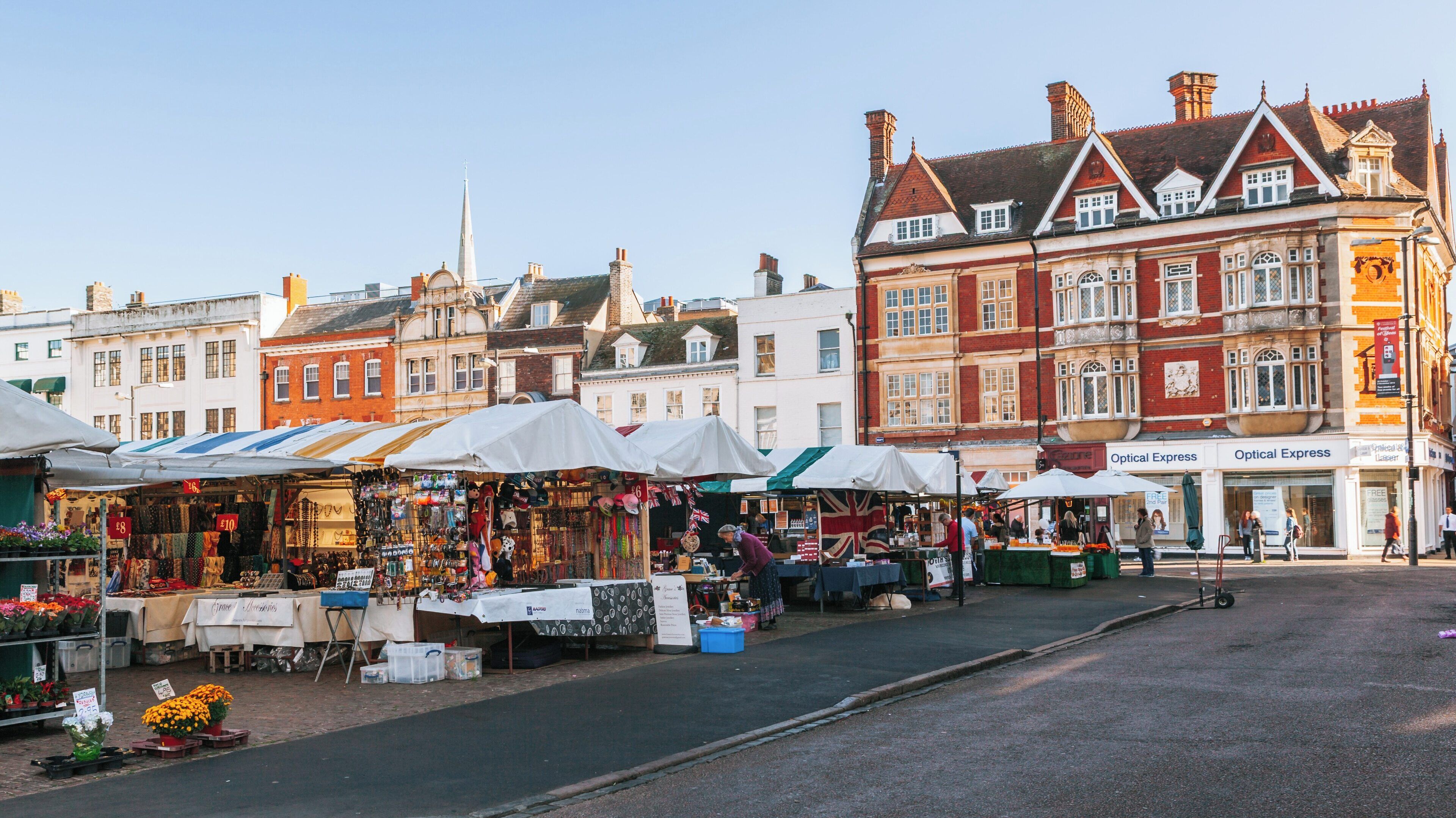 Vibrant market stalls and historic buildings in Cambridge Market Square, bustling with visitors and local vendors in a sunny atmosphere