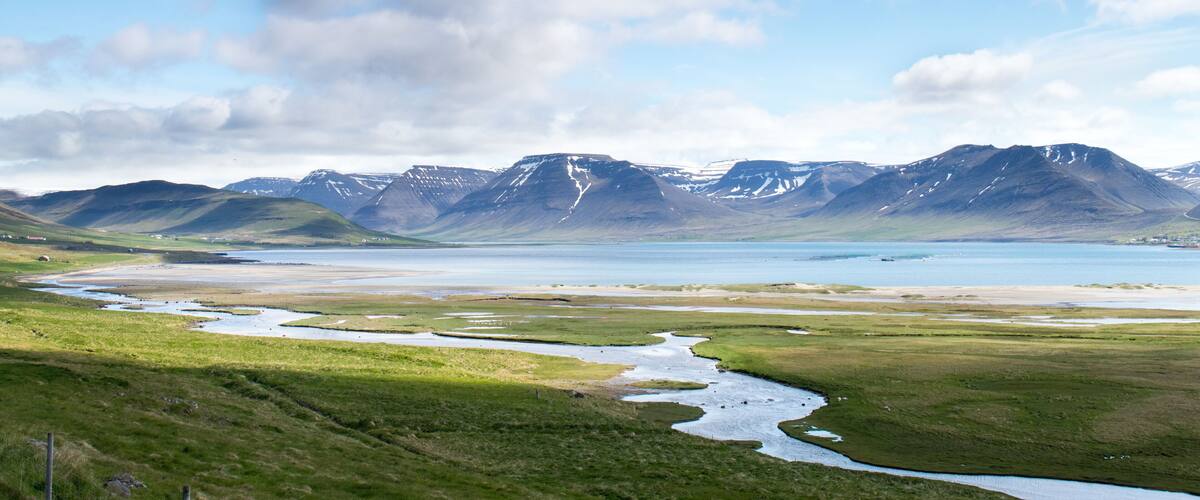 A river flowing through a green valley with mountains in the background.