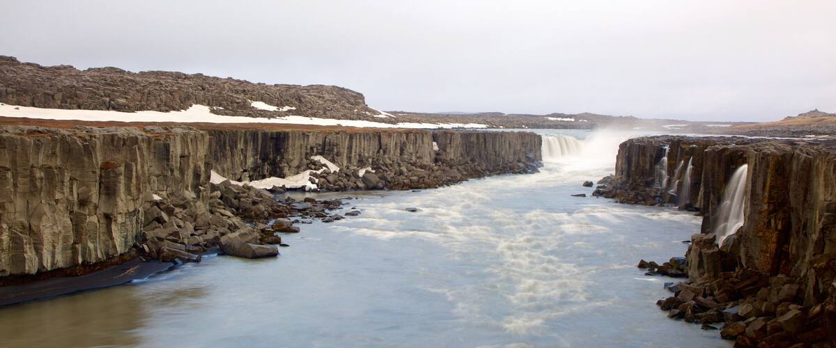 A waterfall cascading down a rocky cliff with snow patches on the ledge.