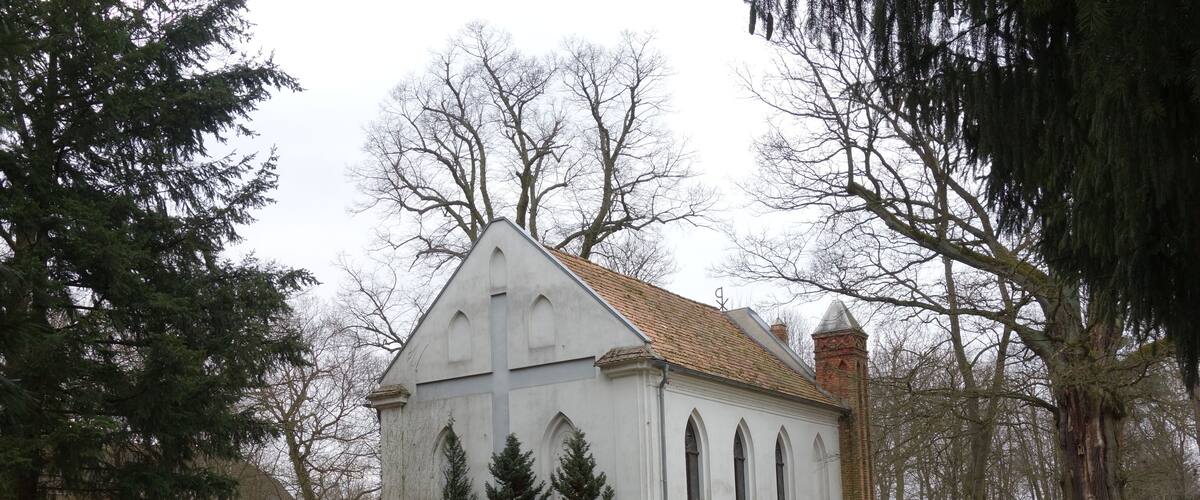 A white church with a tiled roof surrounded by trees and a cemetery.
