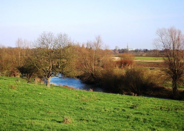 View towards Cambridge View of the River Cam as it flows into Cambridge. The tall spire in the background belongs to the Roman Catholic church on the corner of Lensfield Road and Regent Street. This corner is also known as Hyde Park corner. The farmland is part of the Trumpington Hall Estate.