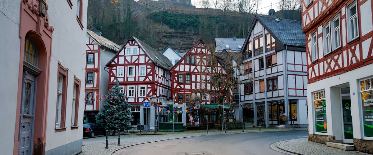 A cobblestone street lined with traditional half-timbered houses, a Christmas tree, and a mountain in the background.
