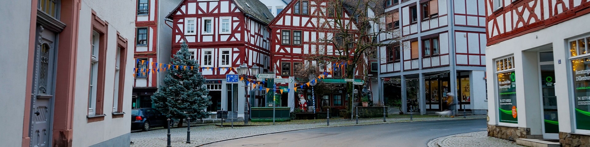 A cobblestone street lined with traditional half-timbered houses, a Christmas tree, and a mountain in the background.