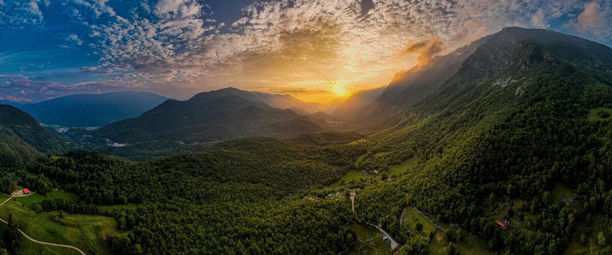 A mountainous landscape with a valley, winding roads, and scattered buildings.