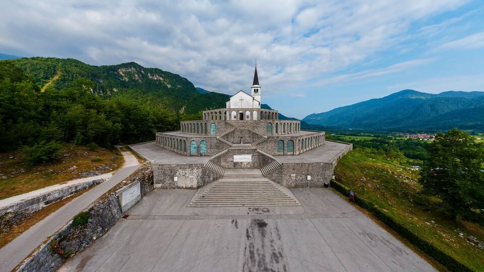 A church with a bell tower surrounded by lush green mountains.
