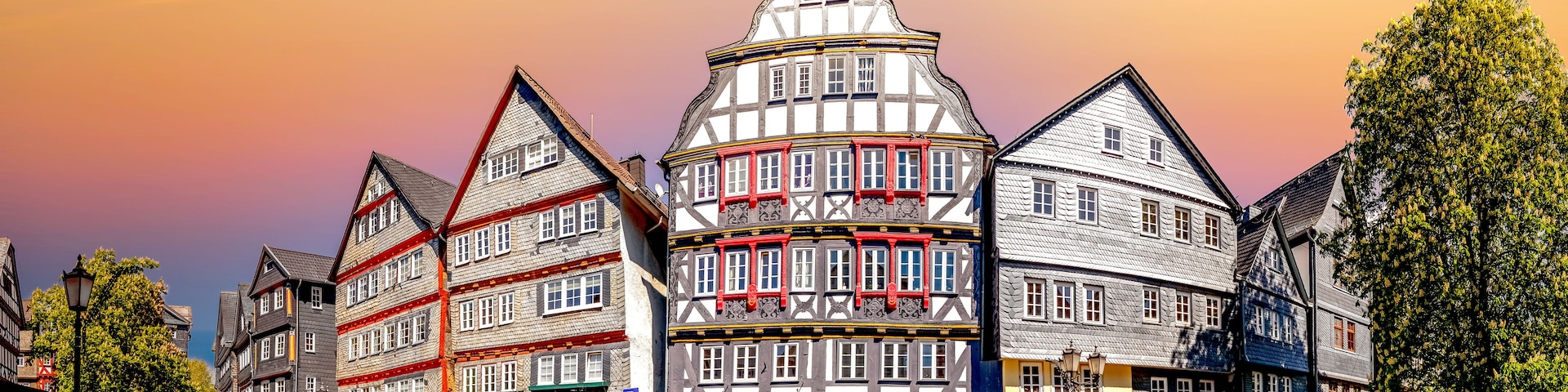 Uma praça europeia com edifícios de arquitetura tradicional em enxaimel, ruas de pedra e carros estacionados.