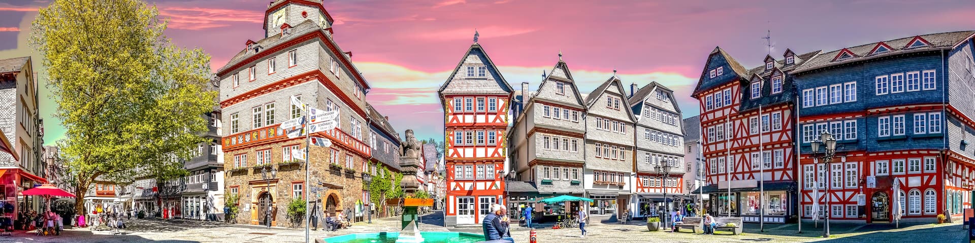 A historic European town square with cobblestone streets, traditional half-timbered buildings, and a fountain.
