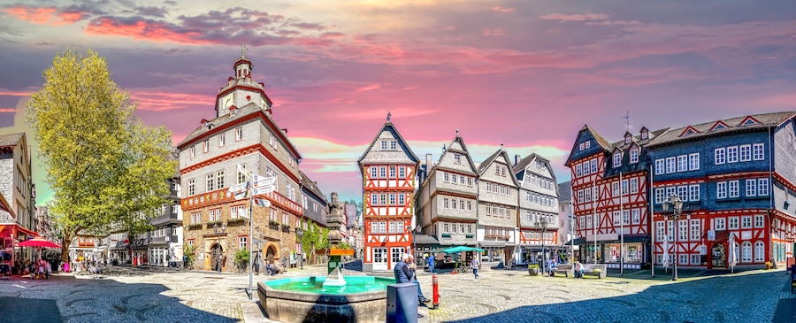 Une place historique au cœur d’une ville européenne, avec ses rues pavées, ses bâtiments traditionnels à colombages et une fontaine.