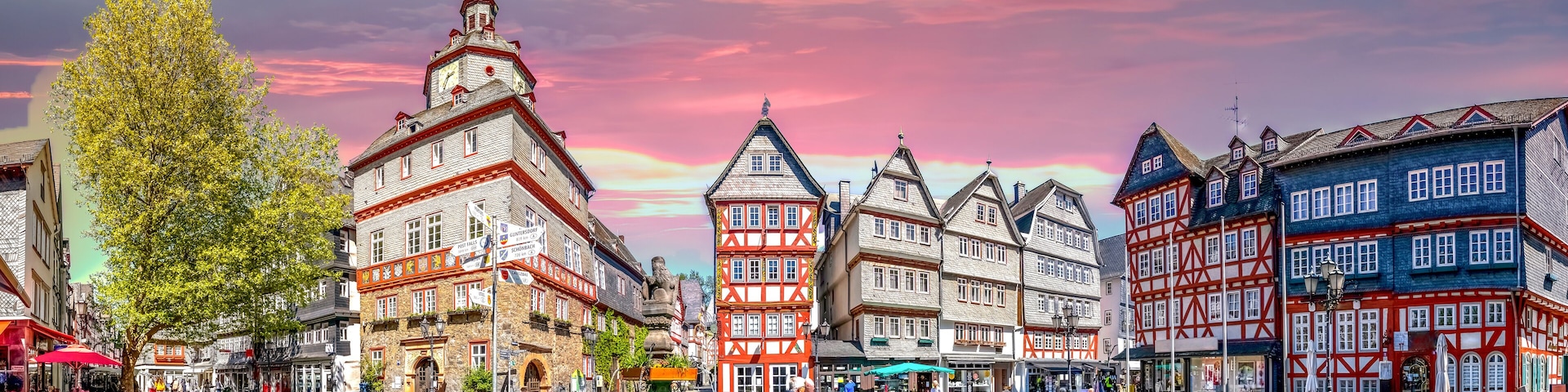 Uma praça histórica europeia, com ruas de pedra, edifícios tradicionais de enxaimel e uma fonte.