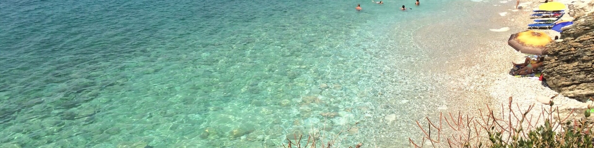 Un mar turquesa transparente, costa rocosa y una playa con sombrillas.
