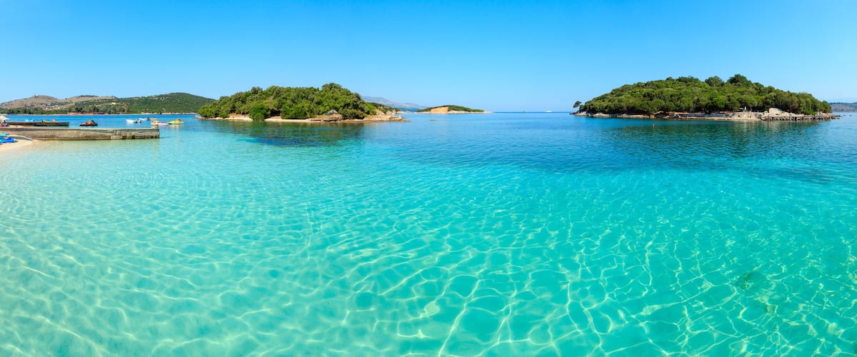 A clear turquoise sea with a sandy beach and small islands with dense greenery.