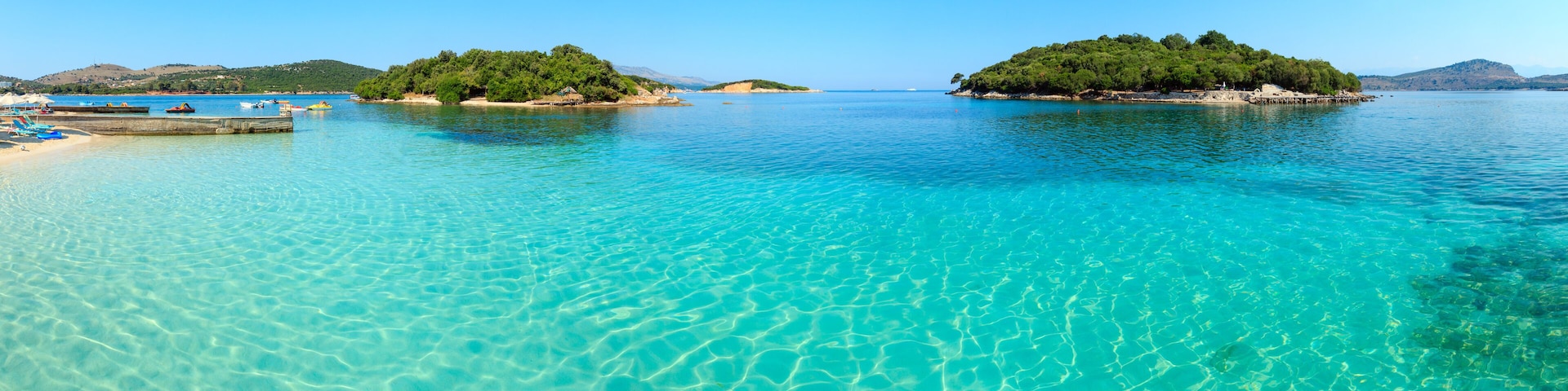 A clear turquoise sea with a sandy beach and small islands with dense greenery.