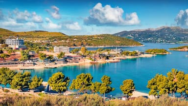 Uma vila costeira com um porto de recreio, águas azuis cristalinas e colinas verdes ao fundo.