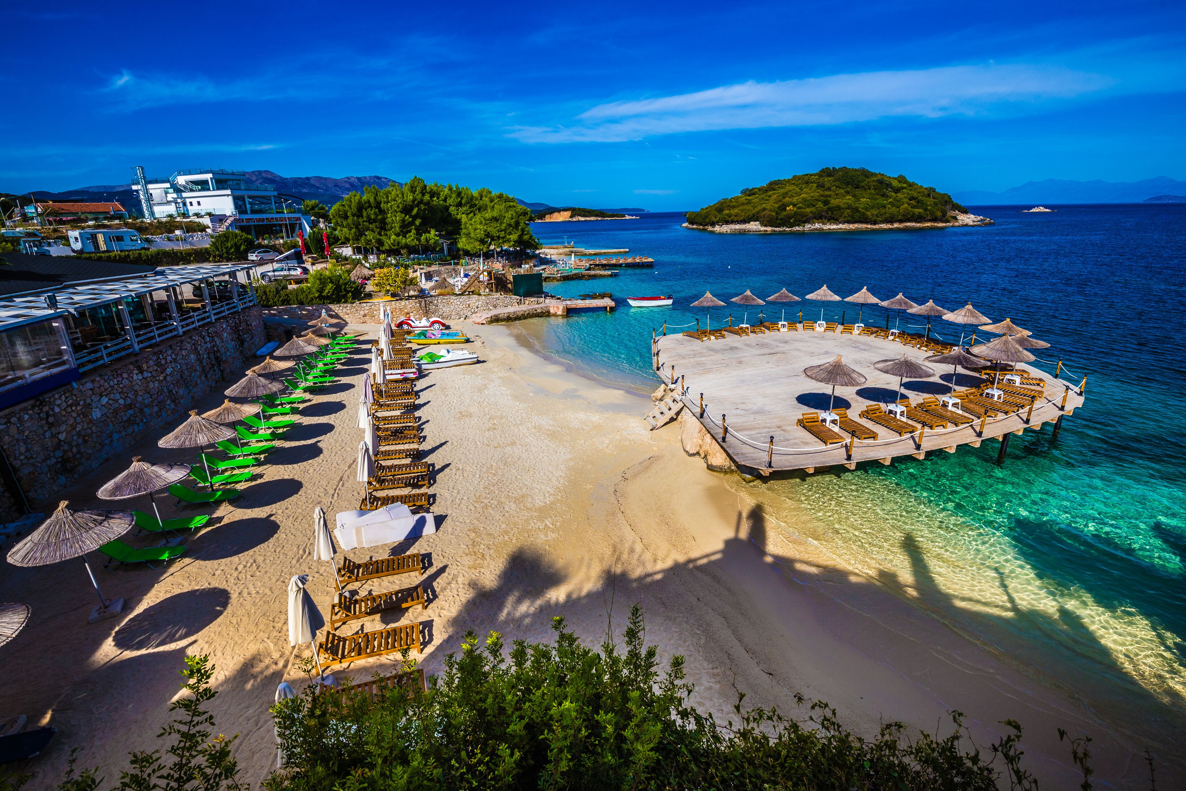 A coastal beach with a pier, umbrellas, lounge chairs, and boats.