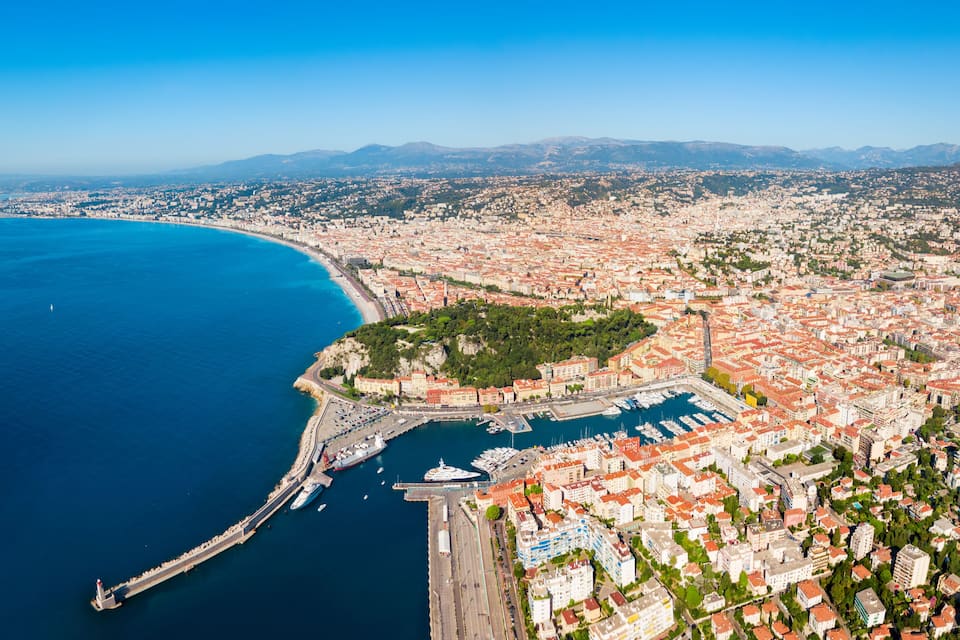 A coastal cityscape with a marina, a prominent lighthouse, and a mountainous backdrop.