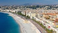 Une ville côtière dotée d’une plage, d’une promenade bordée de palmiers et d’un paysage montagneux en arrière-plan.