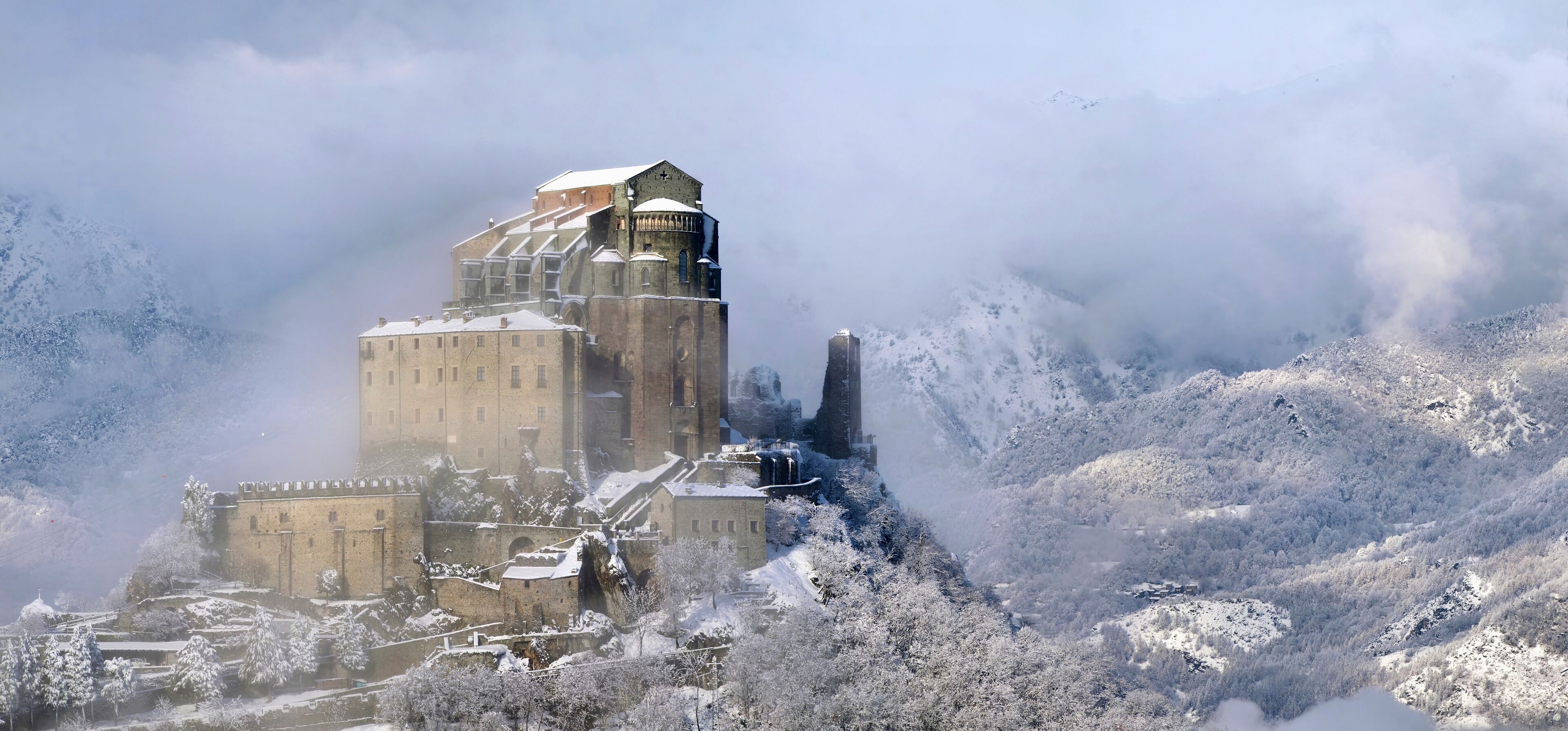 A historic castle surrounded by snow-covered mountains and trees.