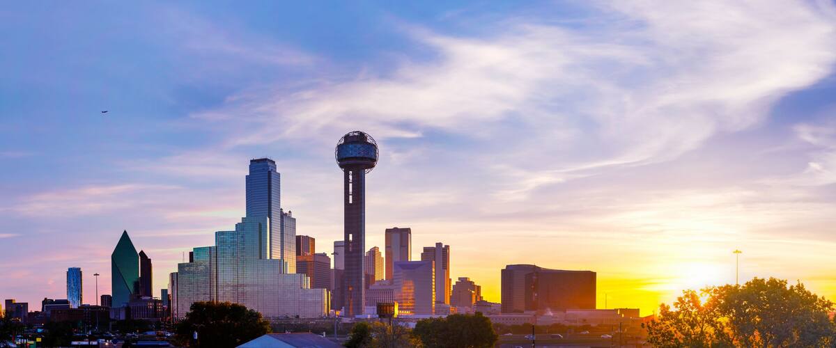 A city skyline with a prominent tower and skyscrapers against a sunset sky.