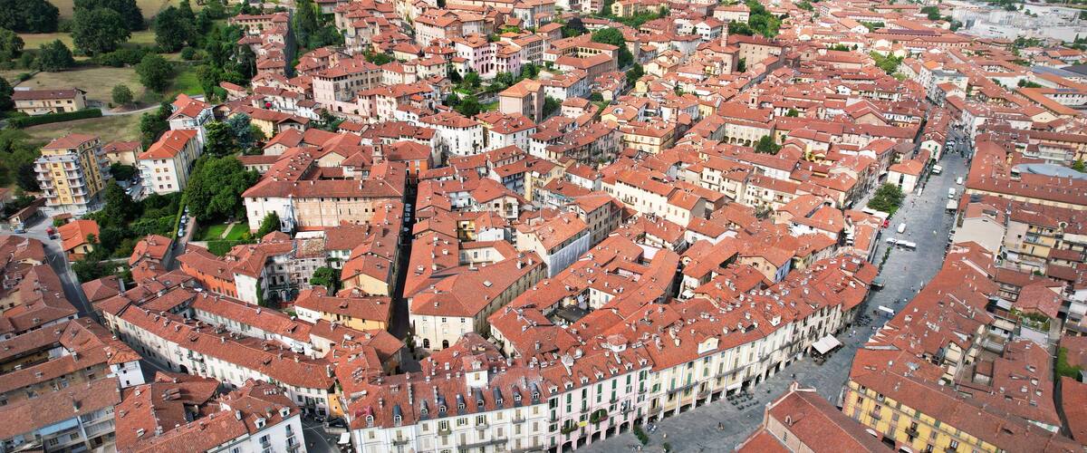 An aerial view of a historic town with red-tiled roofs, a central square, and surrounding greenery.