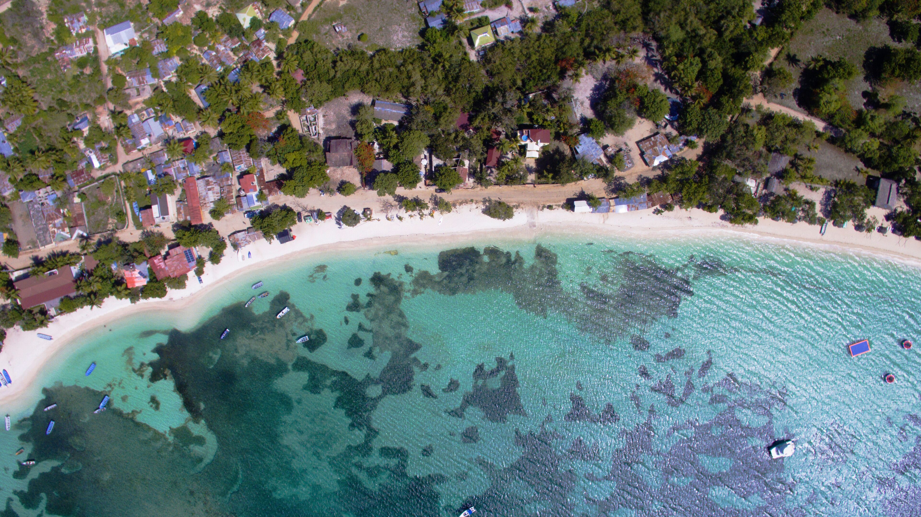 A coastal area with a sandy beach, clear turquoise waters, and scattered boats.