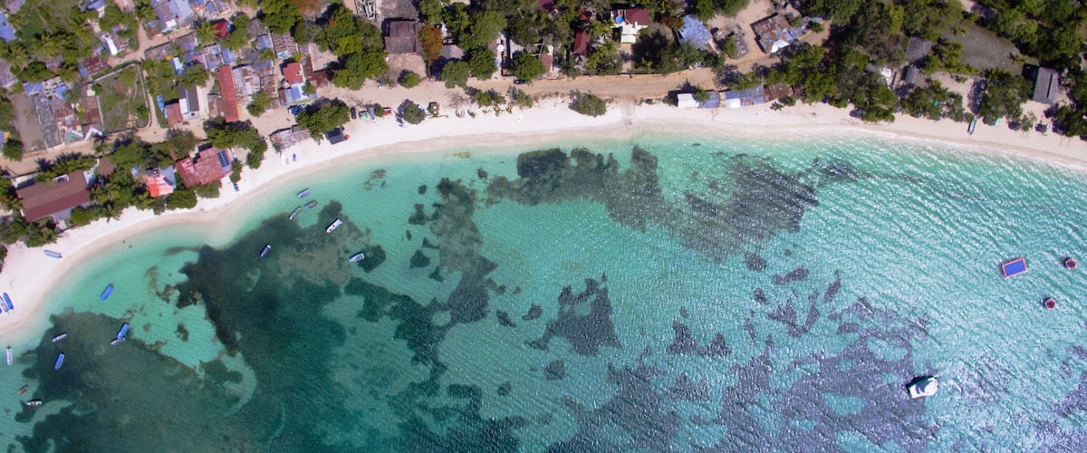 A coastal area with a sandy beach, clear turquoise waters, and scattered boats.
